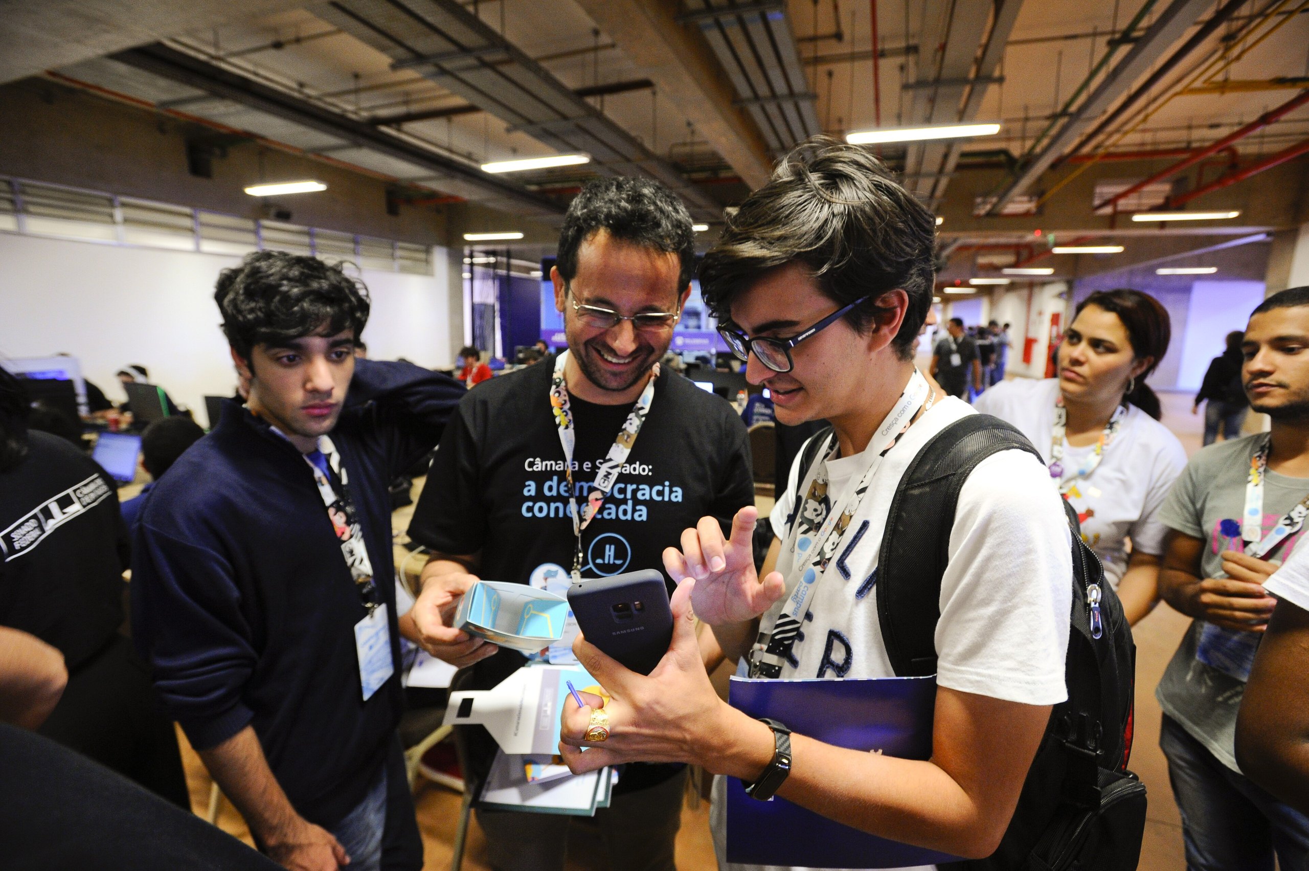 Jovens participantes rindo e interagindo em torno de um projeto de tecnologia num evento no Brasil